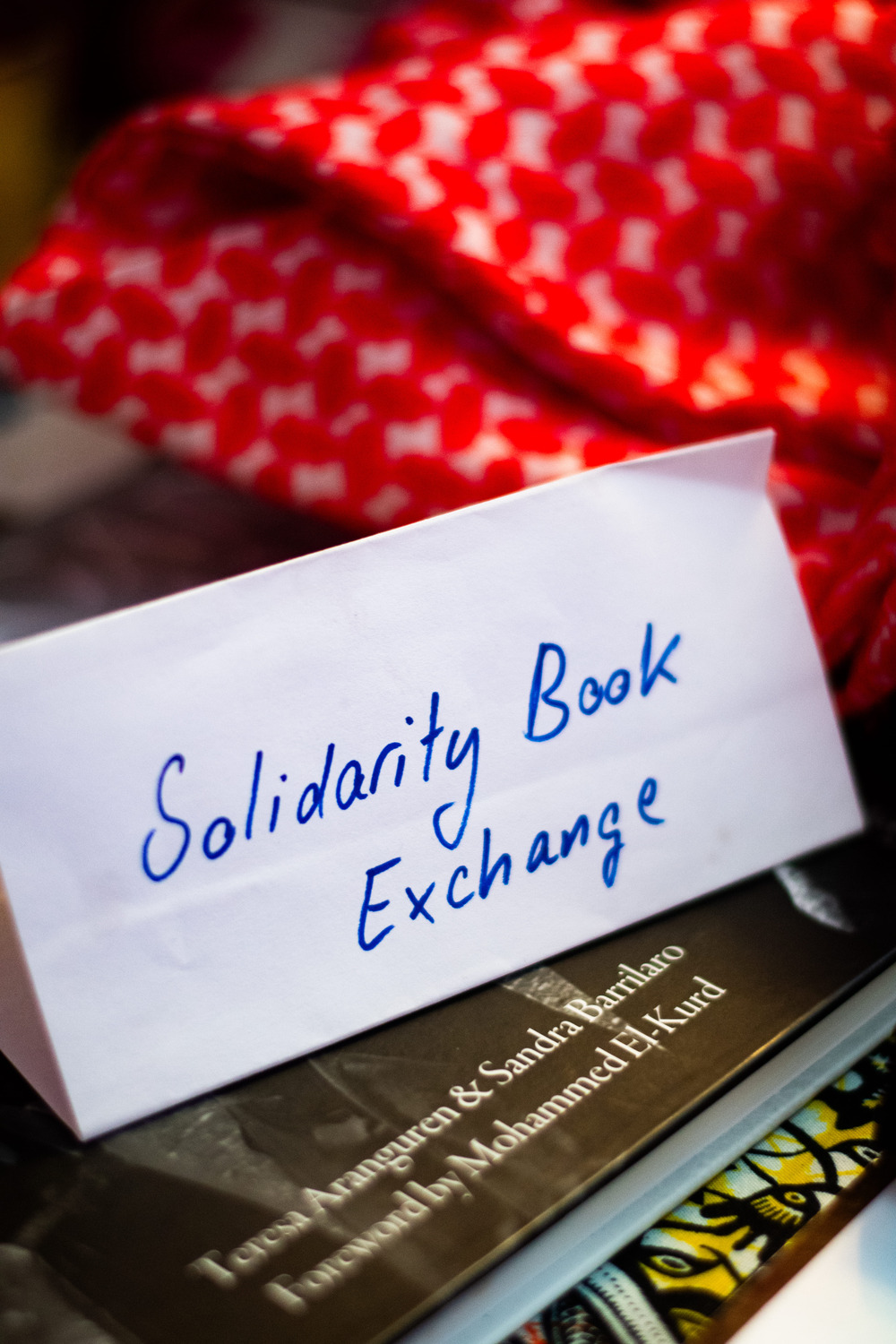 Solidarity Book Exchange sign made on a folded piece of paper sitting ontop of some books