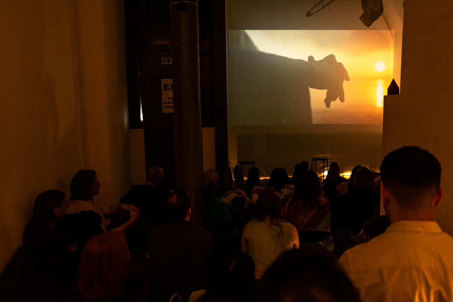 A room full of people sitting on chairs and the floor watching one of the shorts from the 'Al Dar - Shorts from Yemen' screening.