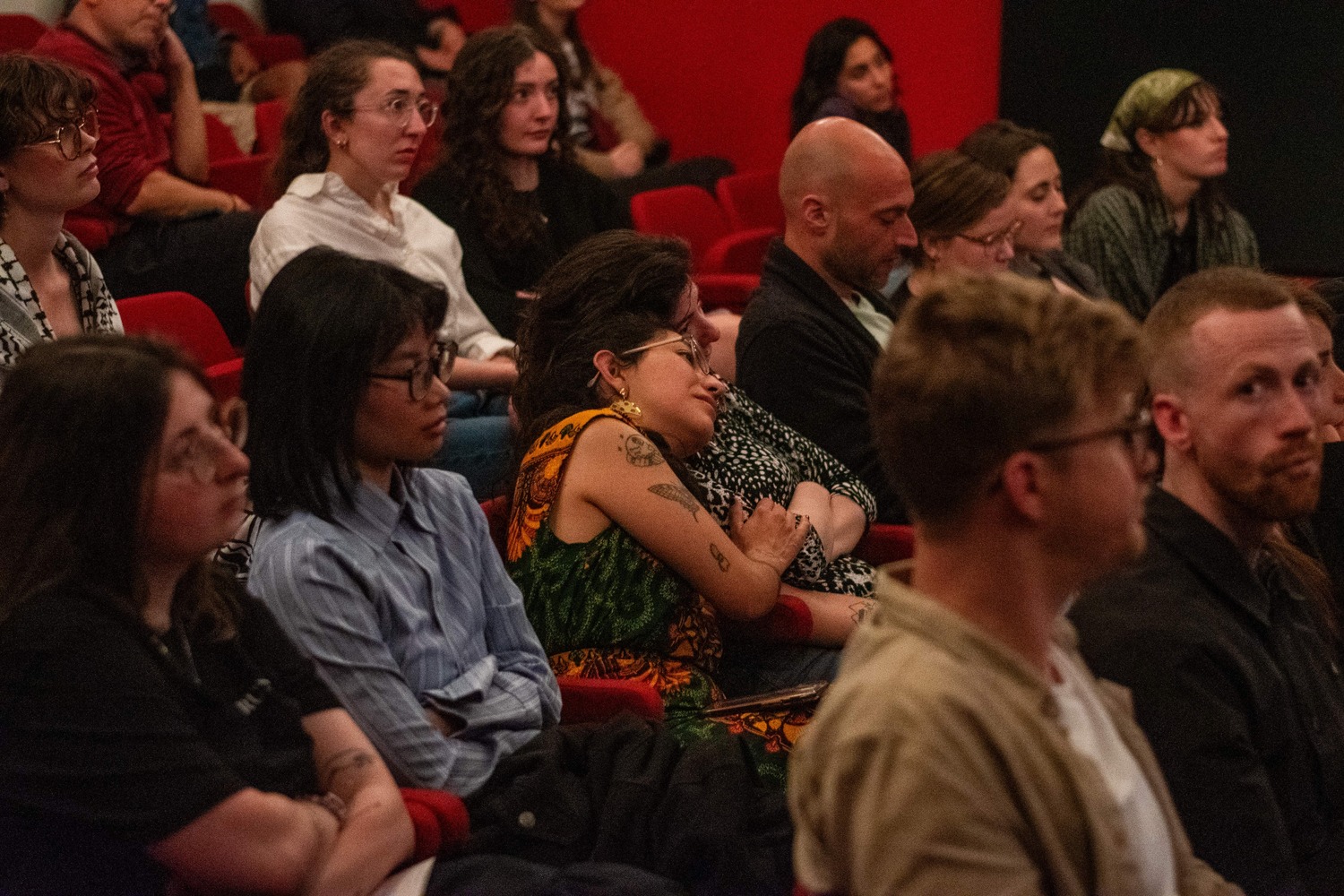 An audience at Falastin Film Festival sitting in red cinema chairs and participating in a Q&A.