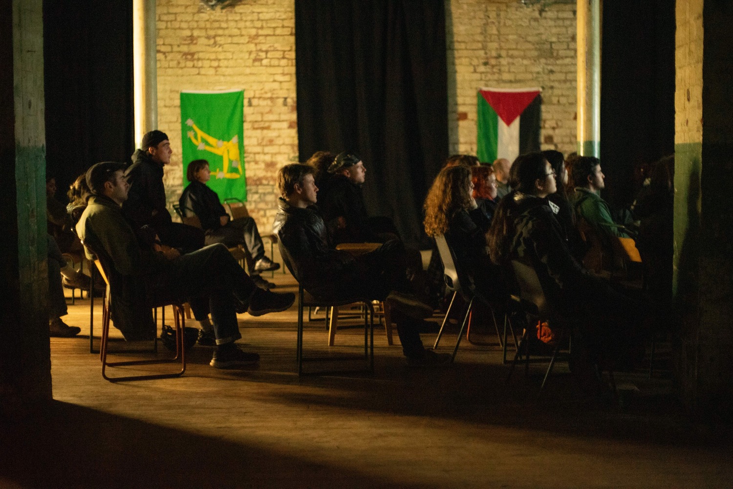 An audience at our 'Solidarity is something you can hold in your hands' screening watching the film while the Palestine flag & the Starry Plough hang in the background