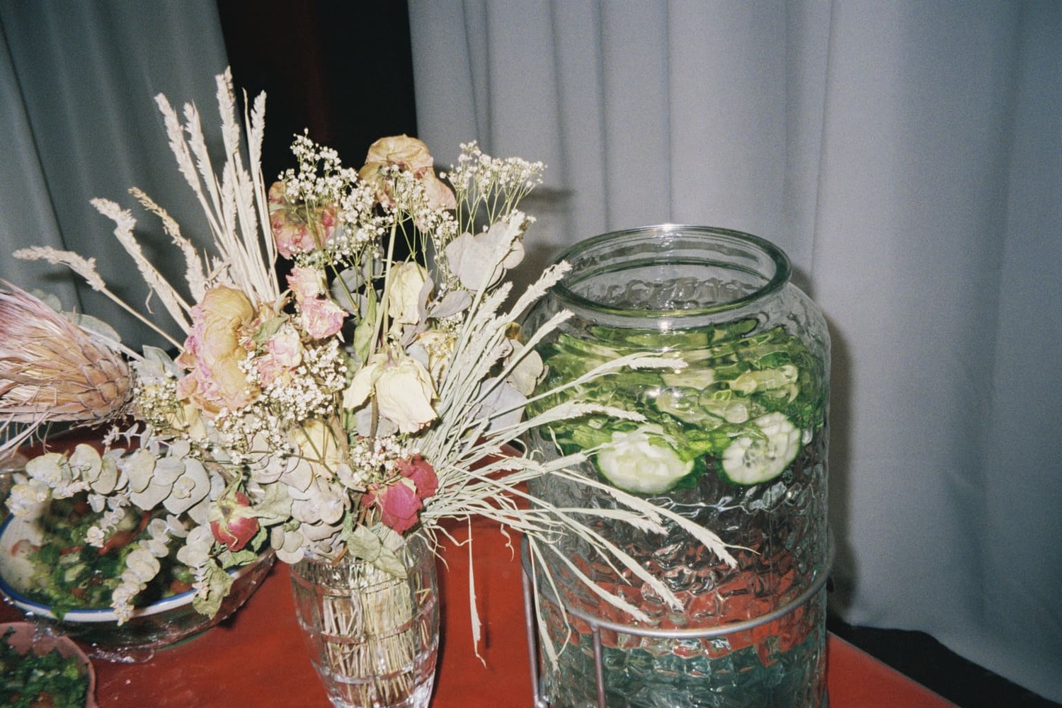 The table with the community meal mainly focused on a vase of flowers and a container of cucumber water.