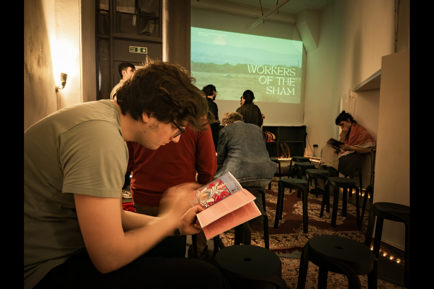 The screening space in the Listen Gallery set up for the Workers of the Sham screening. Community members are getting comfertable while reading Issue 4 of the Solidarity Screenings booklet.